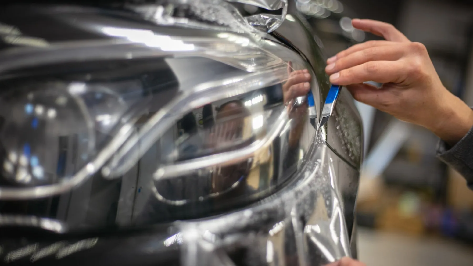 Clear paint protection film being worked over a headlamp by hand